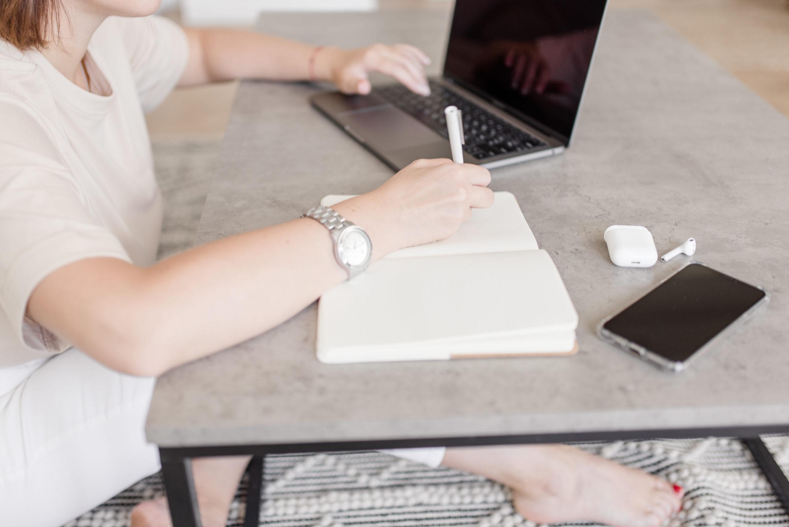 Virtuelle Assistentin sitzt am Schreibtisch mit Block und Laptop
